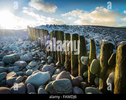 Alte hölzerne Buhne, auf einem Kieselstrand, mit Sonnenlicht strahlte durch die Wolken. Stockfoto