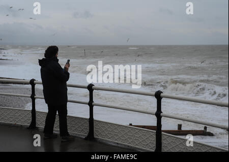 Eine Frau steht auf Worthing Pier und nimmt ein Foto der großen Wellen auf den Strand am Neujahrstag in Worthing, West Sussex, England. Stockfoto
