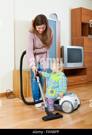 Lächelnde junge Mutter und Baby mit Staubsauger reinigen Wohnzimmer Stockfoto