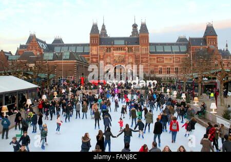 Menschenmenge Schlittschuhlaufen auf der saisonalen Eisbahn am Museumplein (Museumsplatz), Amsterdam, Niederlande. Rijksmuseum auf der Rückseite Stockfoto
