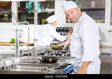 Küchenchef gießt Olivenöl in Pfanne auf eine Profi-Küche Stockfoto