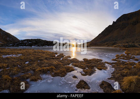 Hoch gelegenen Bergsee im idyllischen Land. Reflexion des Sonnenlichts auf die Eisfläche. Glühende Sunstar am Horizont bei s Stockfoto