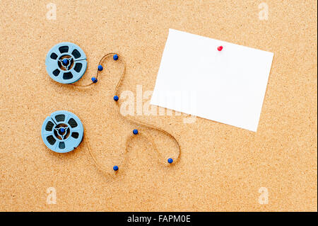 Zwei kleine blaue Film Reel, Filmstreifen und weiße Karte fixiert auf Pinnwand Stockfoto