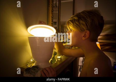 Ein kleiner Junge schaut in eine geheimnisvolle Schüssel mit einem magischen hellen Licht Stockfoto