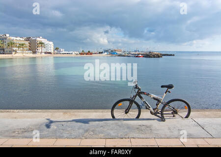Fahrrad geparkt auf dem Pier an der Bucht mit Blick auf Hotels und Marina an einem sonnigen Wintertag im Dezember Stockfoto