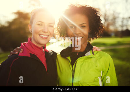 Close-up von zwei jungen Sportlerinnen umarmen und sming an Kamera in Park Stockfoto