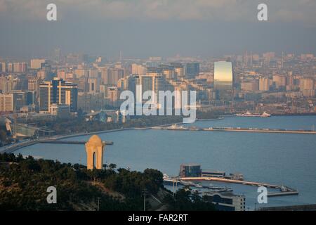 Blick über Baku, Aserbaidschan, und das Kaspische Meer, im Sonnenschein mit Dunst zeigt das 20. Januar-Denkmal im Vordergrund. Stockfoto