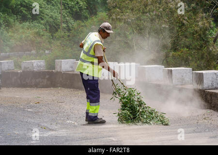 Madeira - Straße durch San Roque de Faial. Arbeiter verwendet einen Zweig als einen Besen, um losen Schotter von der Fahrbahn zu fegen. Stockfoto