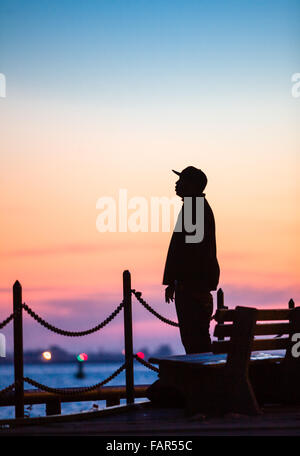 Ein Mann stehend Silhouette gegen den Sonnenuntergang entlang der Uferpromenade. Stockfoto