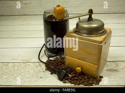 Zwei Kaffeemühlen alte aus Holz und modernen elektrischen Kaffeebohnen auf verstreuten auf Holzbohlen blauer Hintergrund im Stil von v Stockfoto