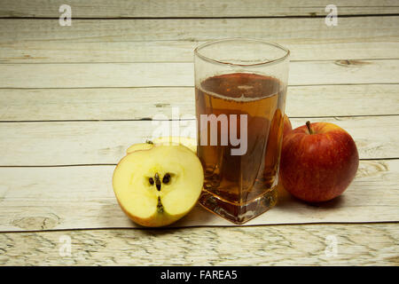 Ein Glas Apfelsaft, einen ganzen Apfel und zwei Apple-Hälften auf einem Holzbrett in bläuliche Farbe der Dielen im Vintage-Stil. Stockfoto