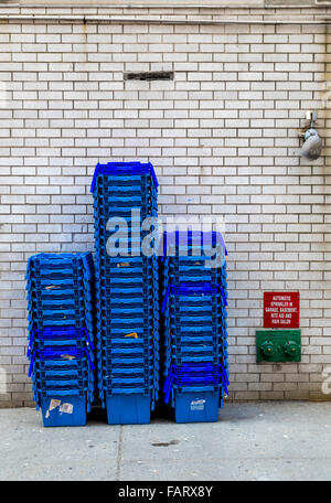 Gestapelte Container auf einem Bürgersteig mit einem Hydranten und Licht vor einer verglasten Wand. Stockfoto