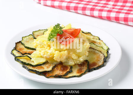 Kreis der dünne Scheiben gebratene Zucchini mit gekochten Kartoffeln, Spiegelei, Tomaten und Petersilie auf einem weißen Teller Stockfoto