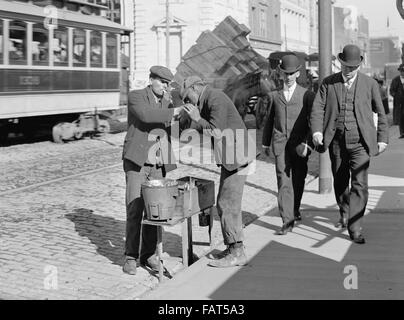 Mann zündet sich eines anderen Mannes Zigarette auf City Street, USA, ca. 1905 Stockfoto