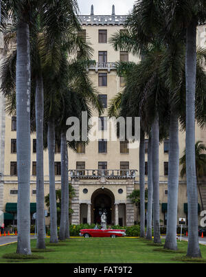 Ein rotes Cabrio wartet zwischen den Palmen & das Hotel Nacional De Cuba, während Touristen abgesetzt werden. Stockfoto