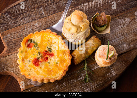 Eine Vielzahl von leckeren herzhaften Kuchen und Snacks serviert auf einem Holzbrett. Stockfoto