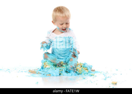 Ein einjähriges Baby junge Zerschlagung einer blauen Geeiste Geburtstagstorte auf einem Holzbrett. Bild wird auf einem weißen Hintergrund isoliert. Stockfoto