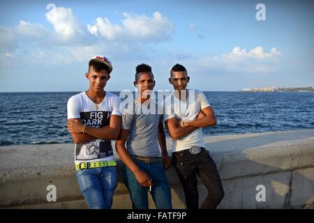 Drei trendige junge kubanische Männer stützte sich auf den Deich, Rauchen eine Zigarette auf dem Malecon Küsten Esplanade in Havanna, Kuba Stockfoto