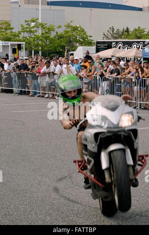 Ein Motorrad-Stunt-Performer begeistert ein kleines Publikum mit einem Wheelie in einem Outdoor-Show-Veranstaltungsort. Stockfoto