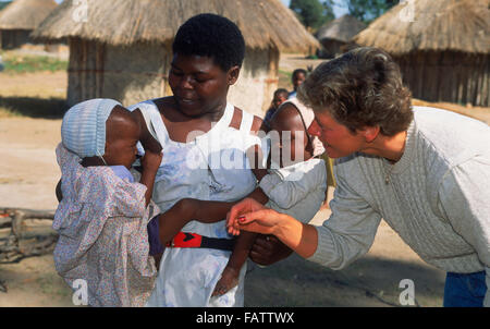 Afrikanerin mit zwei Babys im Arm vor Dorf Hütte in ländlichen Simbabwe mit weibliche Touristen besuchen Stockfoto