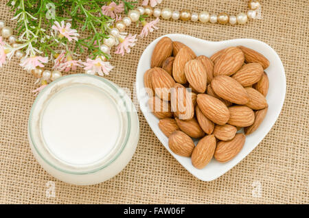 Mandelmilch mit Mandeln auf einer Schüssel weiß Tasse mit Blume auf Sack Hintergrund. Stockfoto