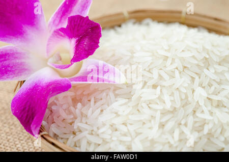 Roher Reis mit violetten Orchidee Blume im Weben Korb auf Sack Hintergrund. Stockfoto