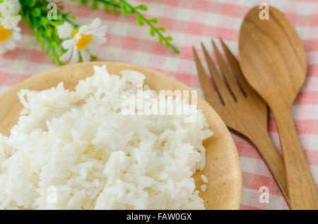 Schüssel mit Reis gekocht und Holzlöffel mit Blume auf Tischdecke. Stockfoto