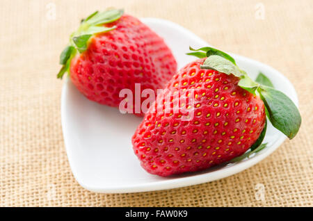 Reife rote Erdbeeren in weiß Tasse Herzform auf Sack Hintergrund. Stockfoto