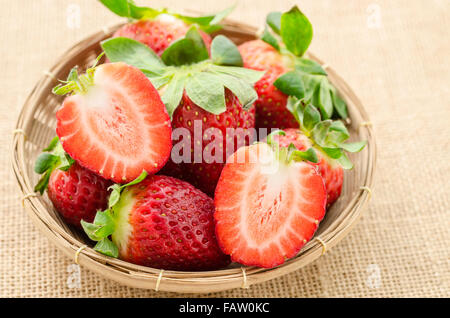 Frische Erdbeeren im Weben Korb auf Sack Hintergrund. Stockfoto