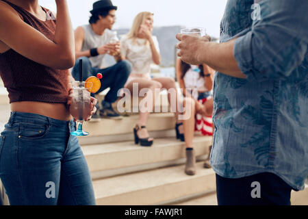 Zugeschnittenen Schuss von ein paar Cocktails Gläser während drei Menschen miteinander zu reden, im Hintergrund halten. Junge Menschen havi Stockfoto