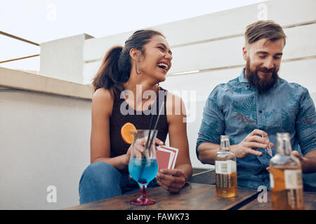 Paar von einem Tisch gefeiert und Spielkarten sitzt. Glückliche junge Mann und Frau Spielkarten während einer Party. Stockfoto