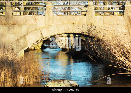 Wölbt sich unter zwei Steinbrücken mit einem kleinen Fluss unterhalb. Reed an den Seiten und ein Stein im Vordergrund. Ende Dezember in Stockfoto