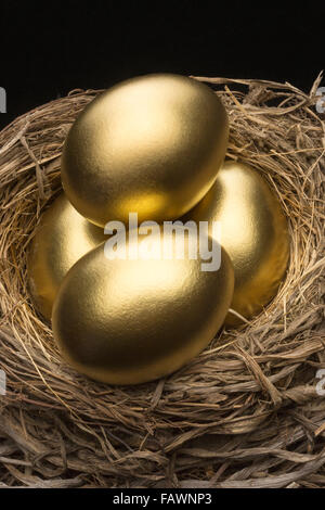 VIER GOLDEN EGGS IM VOGELNEST SCHWARZEN HINTERGRUND Stockfoto