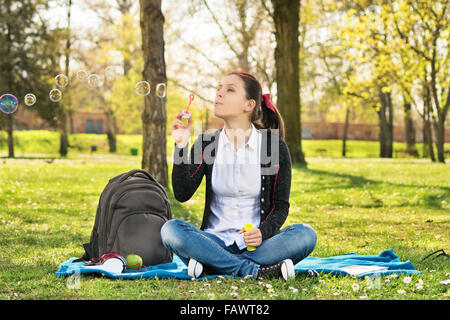 Traum von Wünschen, die durch kommen. Schöne junge Schüler Mädchen sitzt auf einer Wiese bläst Seifenblasen, eine Pause vom Studium. Stockfoto