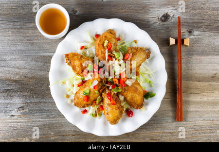 Draufsicht der gebratenen asiatischen Stil Huhn Flügel in weißen Teller mit Beilagen. Grüner Tee und Stäbchen in den Halter. Rustikale Holz boa Stockfoto