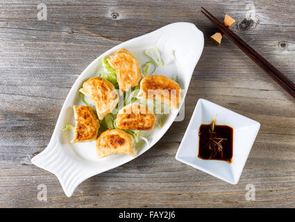 Hoher seitlicher Blick auf chinesische Knödel mit Sauce in Schüssel mit Stäbchen auf rustikalen Holz. Stockfoto