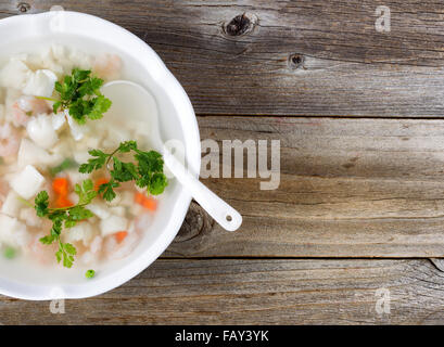 Hoher seitlicher Blick auf Meeresfrüchtesuppe mit Löffel in Schüssel auf rustikalen Holz. Genügend Bewegungsfreiheit Kopie auf der rechten Seite des Bildes. Stockfoto