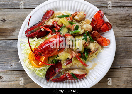 Hoher seitlicher Blick frisch gekochte ganzen Maine-Hummer mit Kräutern, Zwiebeln und Sauce auf weißen Teller bedeckt. Stockfoto