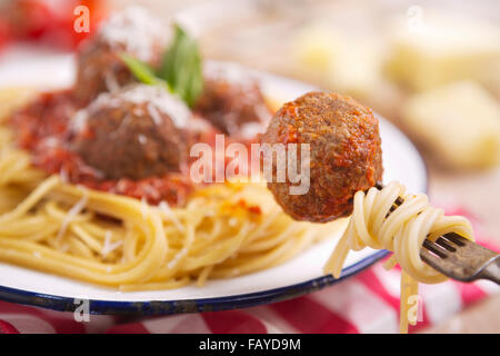 Ein Teller mit Spaghetti mit Fleischbällchen, garniert mit geriebenem Parmesan und Basilikum. Eine Frikadelle ist mit einer Gabel abgeholt. Stockfoto