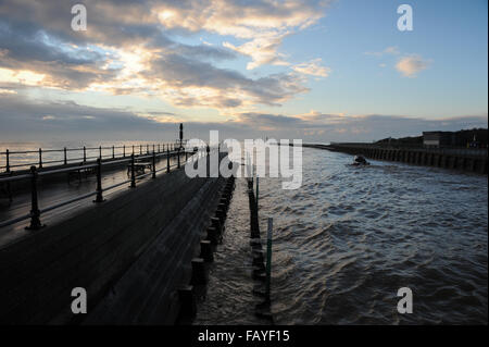 Bei einem wunderschönen Sonnenaufgang, Wolken in den Himmel über dem Meer und hölzernen Pier am Eingang Littlehampton Hafen an der Küste von West Sussex, UK beleuchtet. Stockfoto