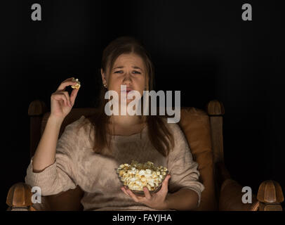 Junge Frau, sitzen im dunklen Zimmer auf der Vorderseite des Fernsehen Film und Essen Popcorn, zeigt Gefühle. Stockfoto