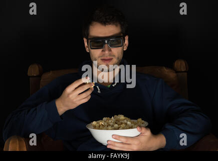 junger Mann sitzt im dunklen Zimmer an der Vorderseite tv Film und Essen Popcorn, 3d Brille Stockfoto