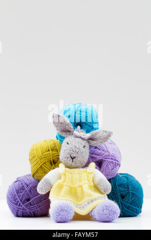 Ein hausgemachtes Kammgarn toy Kaninchen vor der Kugeln aus Wolle sitzen und isoliert auf einem weißen Hintergrund. Stockfoto
