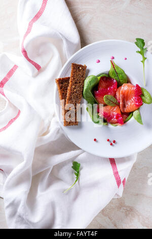 Weiße Keramik-Platte mit Geschnetzeltes Lachs Filet, gesalzen mit rote Beete Saft, serviert mit Vollkorn Toast, Salatblätter und beetr Stockfoto