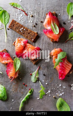 Lachsfilet, gesalzen mit rote Beete Saft, serviert auf Vollkorn Toast mit Salatblättern, Meersalz und Pfeffer über Metall geschnitten Stockfoto