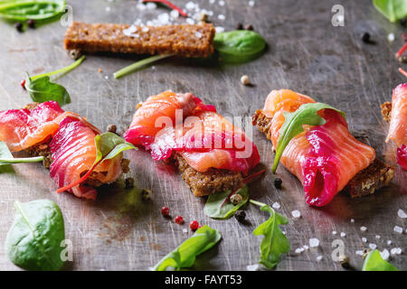 Lachsfilet, gesalzen mit rote Beete Saft, serviert auf Vollkorn Toast mit Salatblättern, Meersalz und Pfeffer über Metall geschnitten Stockfoto