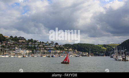 Ein kleines Segelboot überquert den Fluss Dart mit Kingswear steigt im Hintergrund von der Dartmouth höhere Ferry Stockfoto