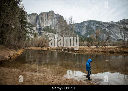 Junges Kind zu Fuß am Ufer des River im Yosemite Valley im Herbst. Tragen einen blauen Wintermantel mit Kapuze. in der Nähe von Wasserfall Stockfoto