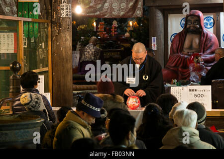 Ein Mönch erhält eine Daruma-Puppe für des Besitzers viel Glück bei der Shorinzan-Daruma-Tempel in Takasaki City, Präfektur Gunma am 6. Januar 2016, Japan zu beten. Besuchen Sie jedes Jahr Tausende von Menschen das Land berühmtesten Daruma Markt (Daruma Ichi) statt am Shorinzan Daruma Tempel am 6. Januar und 7. Takasaki Stadt ist bekannt als die Hauptstadt von Daruma Puppen und etwa 80 % der japanischen Daruma werden dort produziert. Gemäß der Tradition werden ohne Schülerinnen und Schüler auf ihre Augen gemalt Daruma Puppen verkauft. Menschen Farbe in einer Schülerin, wenn ein Wunsch erfolgt zum Ziel gesetzt, wenn der Wunsch geht in Erfüllung oder und das Ziel ist Stockfoto