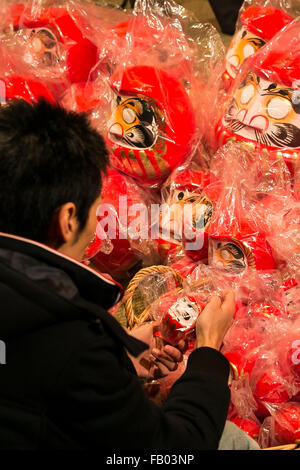 Ein Mann schaut die Daruma Puppen zum Verkauf außerhalb des Shorinzan-Daruma-Tempels in Stadt Takasaki, Präfektur Gunma am 6. Januar 2016, Japan. Besuchen Sie jedes Jahr Tausende von Menschen das Land berühmtesten Daruma Markt (Daruma Ichi) statt am Shorinzan Daruma Tempel am 6. Januar und 7. Takasaki Stadt ist bekannt als die Hauptstadt von Daruma Puppen und etwa 80 % der japanischen Daruma werden dort produziert. Gemäß der Tradition werden ohne Schülerinnen und Schüler auf ihre Augen gemalt Daruma Puppen verkauft. Menschen Farbe in einer Schülerin, wenn ein Wunsch erfolgt zum Ziel gesetzt, wenn der Wunsch geht in Erfüllung oder und das Ziel ist erreicht sie f Stockfoto